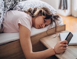 A woman checks her phone while lying in bed.