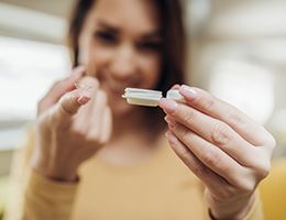 A woman holding a contact lens on the end of one finger and a lens case in her other hand.