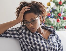 A sad woman with a Christmas tree in the background.