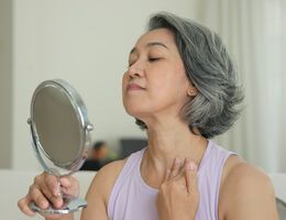 A woman holds a mirror as she examines her throat.