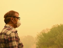 A man in a face mask stands outside on a smoky day.