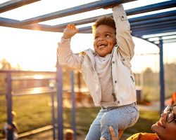  Kid going across monkey bars with mom holding on to them from below.