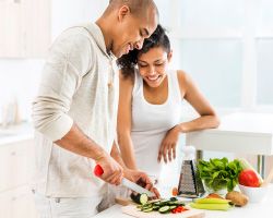 A couple cutting fresh vegetables at a kitchen counter.