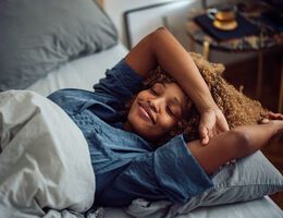 A smiling woman leans back on her pillows in bed.