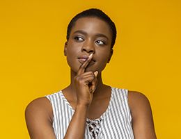 A young woman holds her finger to her mouth in deep thought.