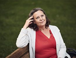 An older woman sitting with her hand pressed against her forehead.