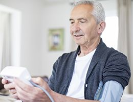 An older man using a blood pressure monitor at home.
