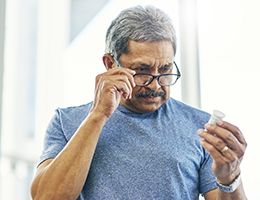 Older man with reading glasses looks at a pill bottle.