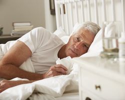 Man lying in bed holding a tissue and looking unwell.