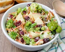 A bowl with a salad made up of creamy broccoli, apple, and various veggies.