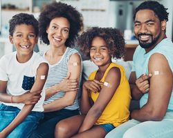 A man, woman and two children smile and display bandages on their upper arms.