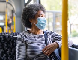 A woman wearing a face mask looks out the window of a bus.
