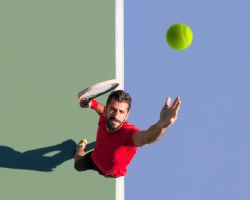 A tennis player tosses a ball up for a serve.