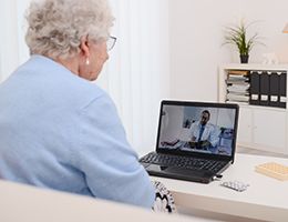 A woman looks at a laptop with a clinician on screen.