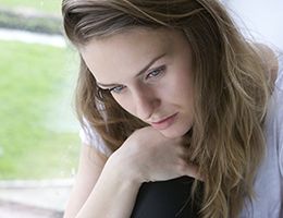 A woman with a somber expression sitting inside her home.