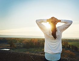 A woman stretches her arms while looking out over a valley.