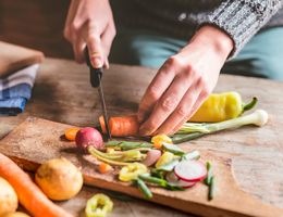 A pair of hands chop vegetables on a wood cutting board.