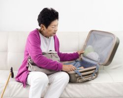 Elderly woman sitting on couch and packing luggage.