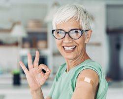 An older woman with an adhesive bandage on her arm makes the OK sign.