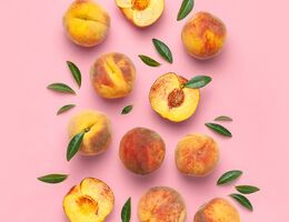 Whole and halved peaches and leaves on a pink background.