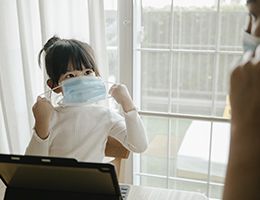 A little girl putting on a face mask.