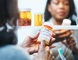 A woman looks at a prescription pill bottle in front of a medicine cabinet.