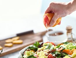 Someone is squeezing a lemon and juice is pouring onto a bowl of salad.