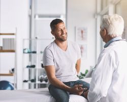 A man sits on an exam table and talks to a doctor