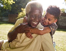 A grandson is hugging his grandfather's neck. Both are laughing.