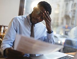 A man sitting at his work desk with his hand pressed against his forehead.