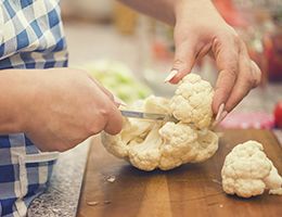 A pair of hands chop cauliflower on a cutting board.