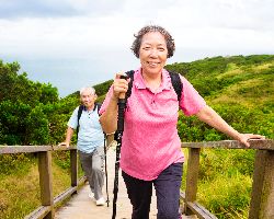 An older couple uses hiking poles on a boardwalk over a marsh.