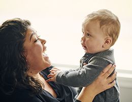 A smiling mom holds up her baby.