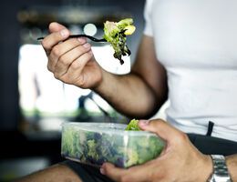 Close-up of a man's hands as he eats salad out of a plastic container with a plastic fork.