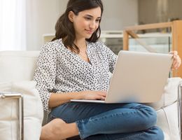 A woman sits on a couch with a laptop.
