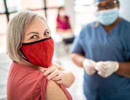A woman wearing a mask and holding up her sleeve to get a vaccine.