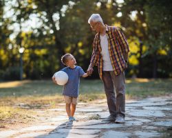 Grandpa walking alongside kid holding ball.