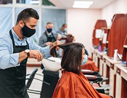 Stylists in a salon, at a safe distance apart, wearing masks and cutting hair.