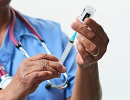 A healthcare worker's hands drawing vaccine from a vial.