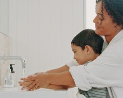 A woman helps a young boy wash his hands.