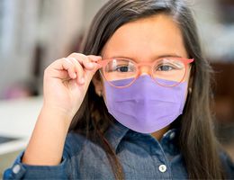 A young child wearing pink glasses and a purple mask.