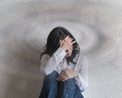 A woman site with her arm around her knees and an hand to her head. The background swirls around her head.