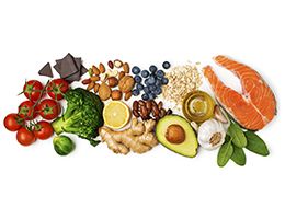 An assortment of heart healthy foods, including tomatoes, chocolate, broccoli, Brussels sprouts, nuts, lemon, ginger, blueberries, beans, ginger, avocado, oatmeal, olive oil, garlic, spinach and fish.