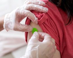 Gloved hands place a small bandage on a person's upper arm.