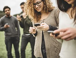 A group of teens standing around all looking at their phones.
