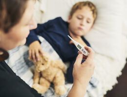  A woman looking a thermometer as a young boy lies in bed with a teddy bear