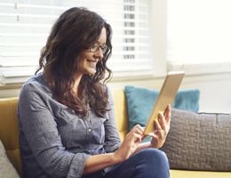A woman sits on a couch using a tablet.