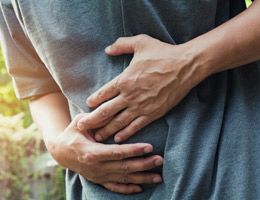 A closeup of someone's lower torso with their hands cradling their stomach. 