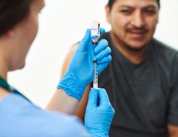 A healthcare worker draws vaccine from a vial while a patient waits.