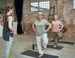 Three older adults stand on one leg as a fitness instructor watches.